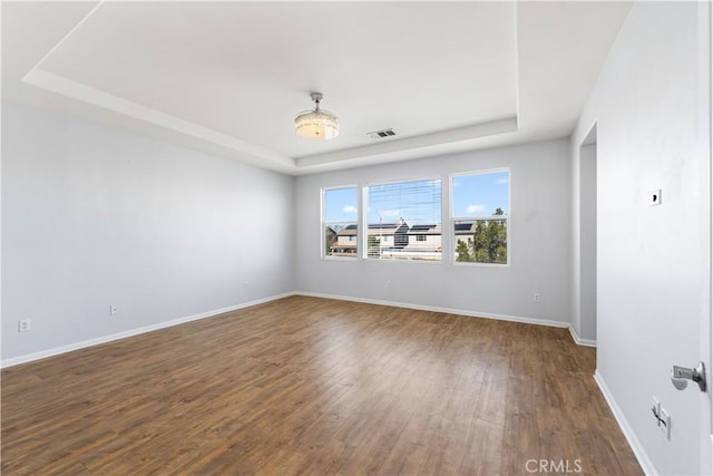 unfurnished room featuring a tray ceiling, wood finished floors, visible vents, and baseboards