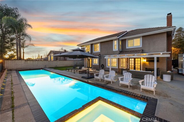 pool at dusk with an outdoor living space with a fire pit, a patio area, a fenced backyard, and a pool with connected hot tub