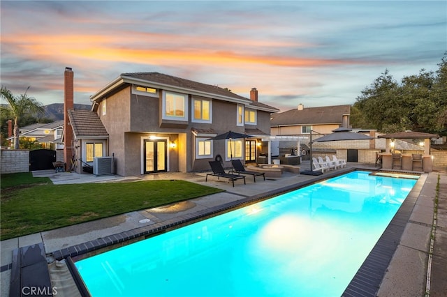 rear view of property with a yard, a chimney, outdoor dry bar, central AC, and a fire pit