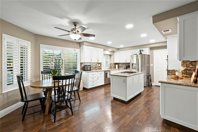 kitchen with stainless steel appliances, decorative backsplash, dark wood-type flooring, white cabinetry, and a kitchen island