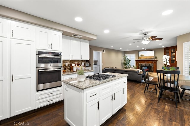 kitchen featuring stainless steel appliances, dark wood-type flooring, a glass covered fireplace, and visible vents