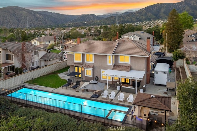 rear view of property with a fenced in pool, a fenced backyard, a mountain view, an outdoor living space, and stucco siding