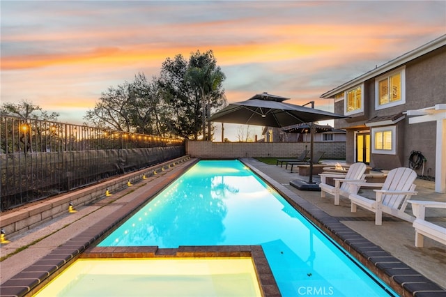 pool at dusk featuring a patio area, a fenced backyard, and a pool with connected hot tub