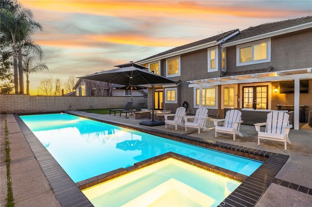 pool at dusk with french doors, a patio area, a fenced backyard, and a pool with connected hot tub
