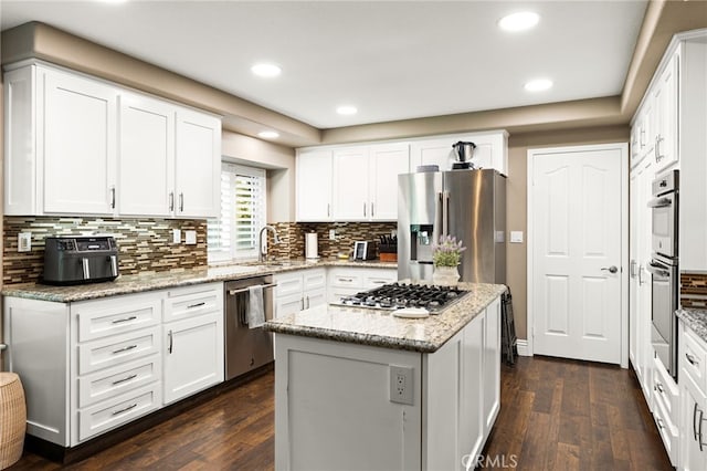 kitchen featuring dark wood-style flooring, backsplash, appliances with stainless steel finishes, white cabinets, and a kitchen island