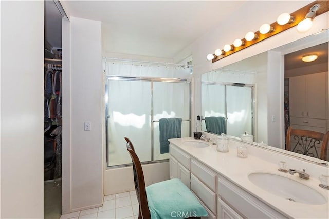 full bath with double vanity, combined bath / shower with glass door, a sink, and a walk in closet