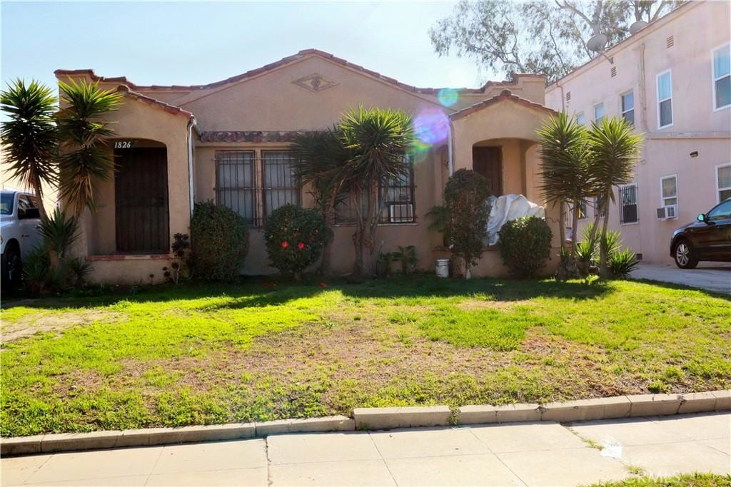 mediterranean / spanish-style house with a tiled roof, a front yard, and stucco siding