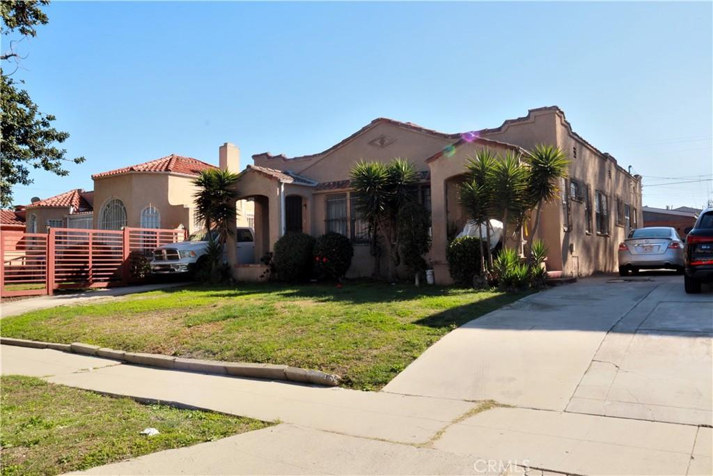 mediterranean / spanish-style home with a tile roof, driveway, stucco siding, a front lawn, and a chimney