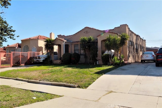 mediterranean / spanish-style home with a tile roof, driveway, stucco siding, a front lawn, and a chimney