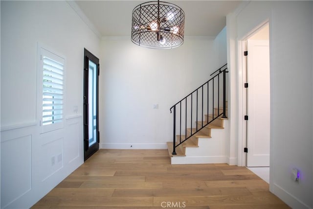 entryway featuring ornamental molding, light wood finished floors, stairs, and baseboards