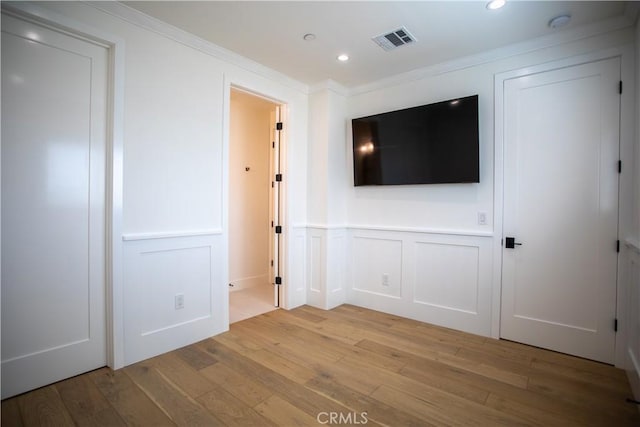 empty room with light wood-type flooring, visible vents, crown molding, and a decorative wall