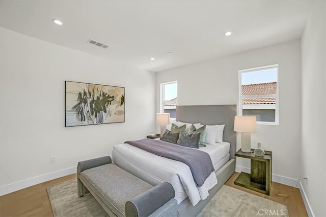 bedroom with wood finished floors, visible vents, baseboards, and multiple windows