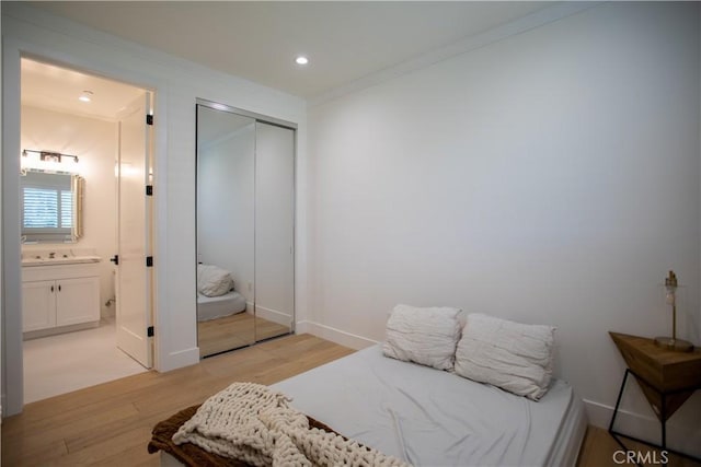 bedroom featuring light wood finished floors, recessed lighting, a closet, ornamental molding, and ensuite bath