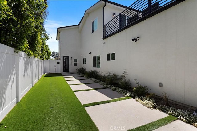 rear view of property with a patio area, fence, a lawn, and stucco siding