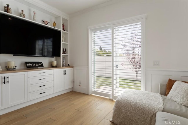 bedroom with light wood-style floors, a decorative wall, ornamental molding, and a wainscoted wall
