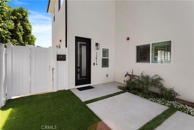 entrance to property with a yard, stucco siding, and fence