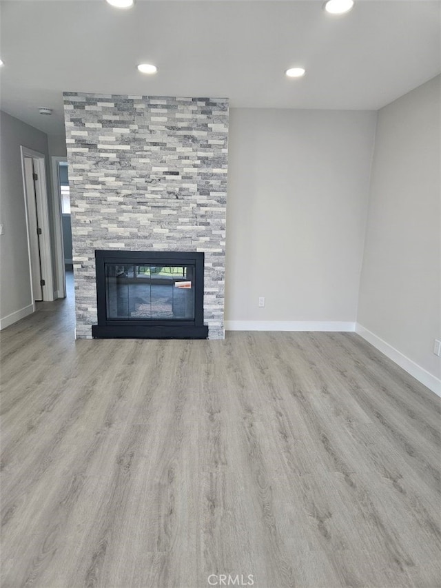 unfurnished living room with wood finished floors, a tile fireplace, and baseboards