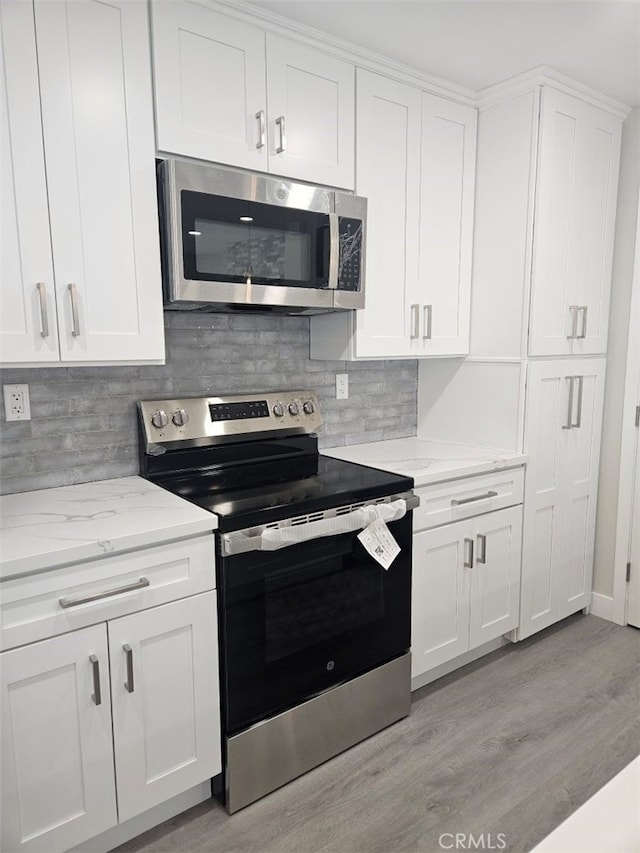 kitchen featuring white cabinetry, appliances with stainless steel finishes, light wood-type flooring, backsplash, and light stone countertops