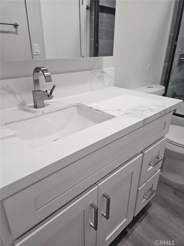 bathroom with toilet, a shower, wood finished floors, and vanity