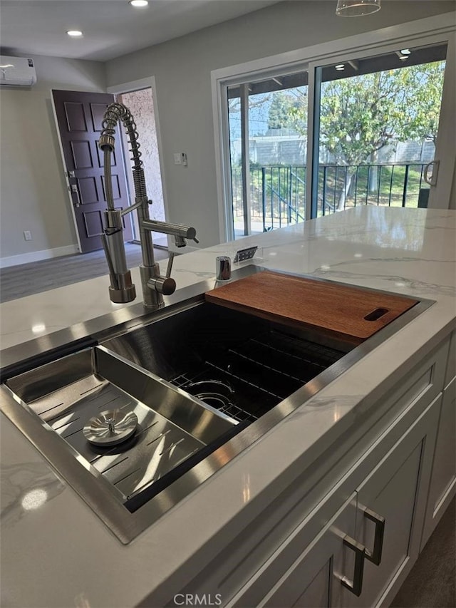 kitchen featuring light stone countertops, baseboards, an AC wall unit, and recessed lighting