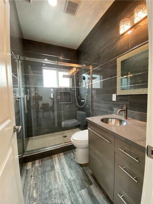 full bathroom featuring a stall shower, visible vents, toilet, vanity, and tile walls