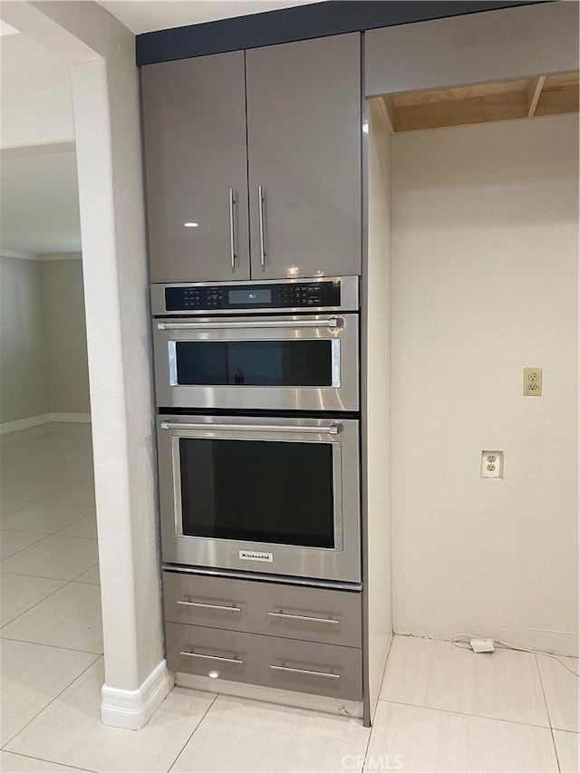 kitchen with light tile patterned floors, double oven, baseboards, and gray cabinetry