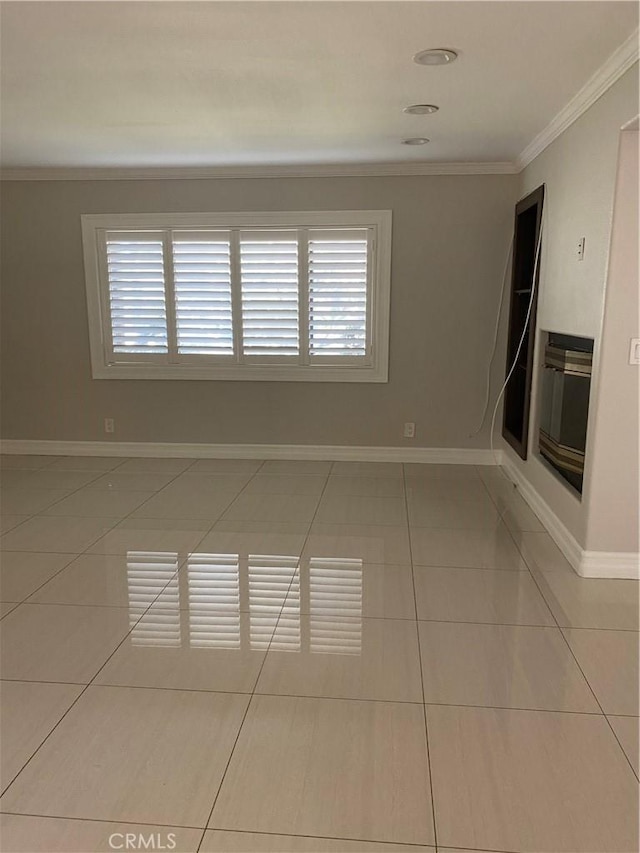 empty room featuring light tile patterned flooring, crown molding, and baseboards