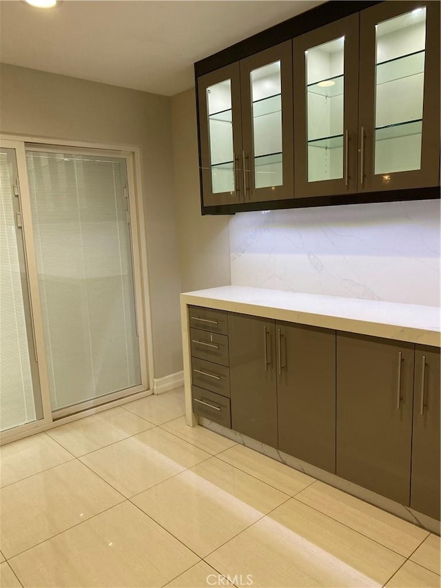 interior space with light countertops, light tile patterned flooring, gray cabinets, and glass insert cabinets