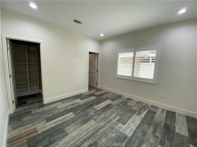 unfurnished bedroom with baseboards, dark wood-style floors, a walk in closet, a closet, and recessed lighting