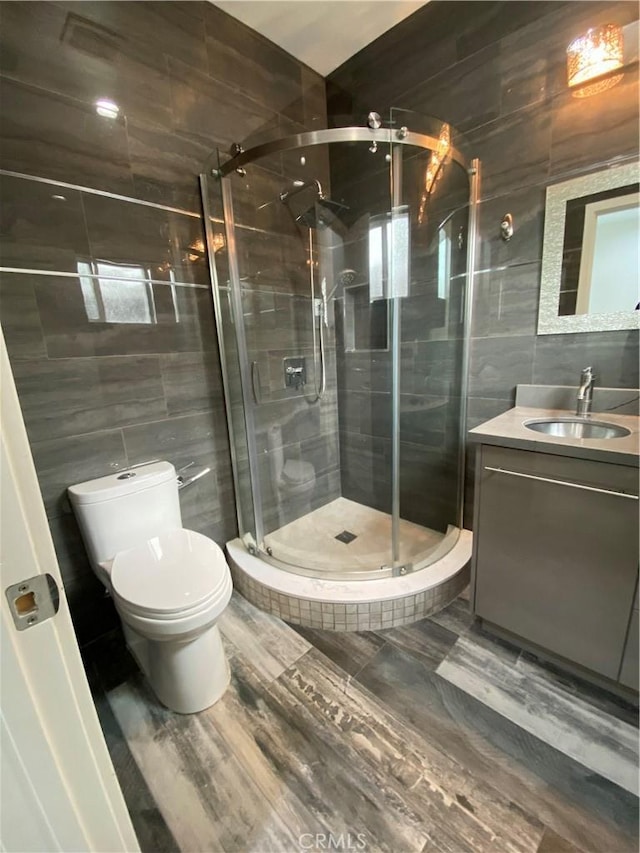 bathroom with a stall shower, toilet, tile walls, and vanity