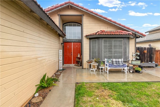 entrance to property with a patio area, a tile roof, and fence