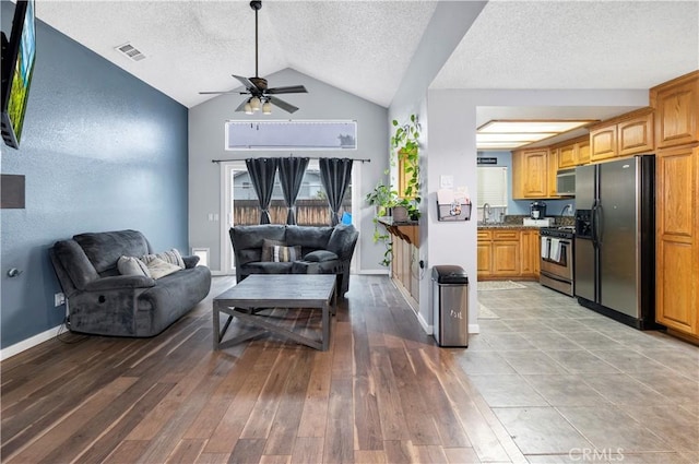 living room featuring light wood-type flooring, visible vents, a textured ceiling, baseboards, and vaulted ceiling