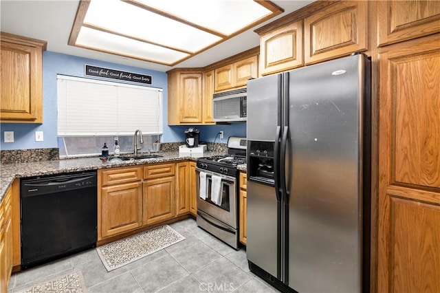 kitchen featuring brown cabinets, a sink, stainless steel appliances, dark stone counters, and light tile patterned floors