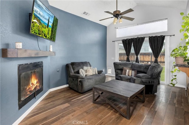 living area featuring vaulted ceiling, visible vents, a warm lit fireplace, and wood-type flooring