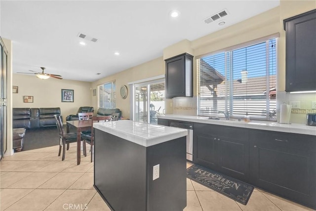 kitchen with tile countertops, light tile patterned flooring, a kitchen island, a sink, and dishwasher