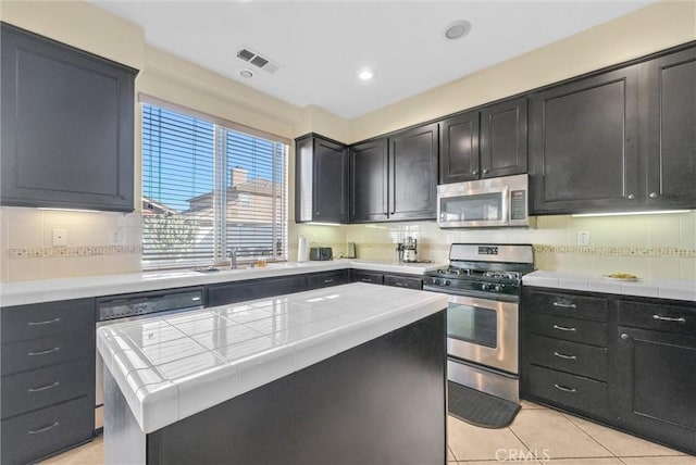 kitchen featuring dark cabinetry, tile counters, stainless steel appliances, and decorative backsplash