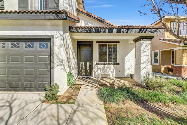 doorway to property with a tile roof, stucco siding, covered porch, concrete driveway, and a garage