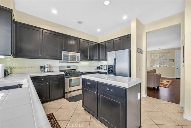 kitchen featuring appliances with stainless steel finishes, light tile patterned flooring, tile counters, and tasteful backsplash