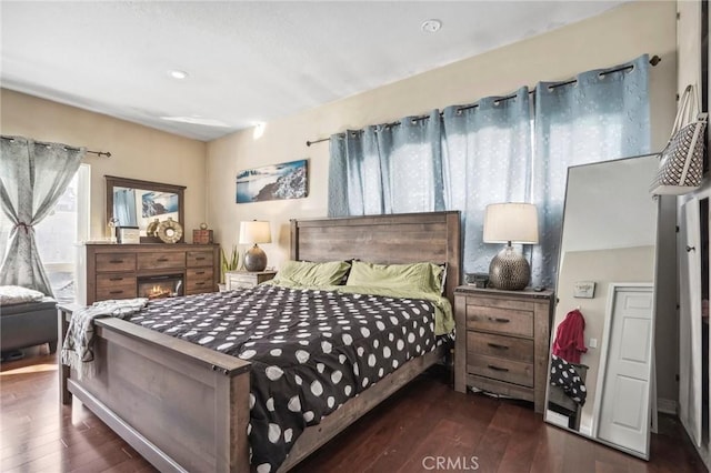 bedroom with a glass covered fireplace and wood finished floors