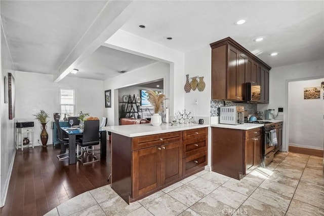 kitchen with decorative backsplash, a peninsula, gas range oven, and light countertops