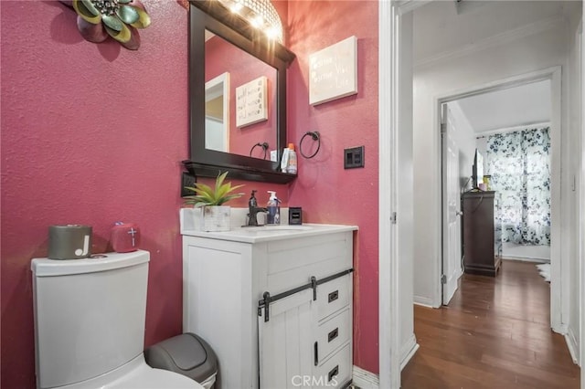 bathroom with vanity, toilet, wood finished floors, and a textured wall