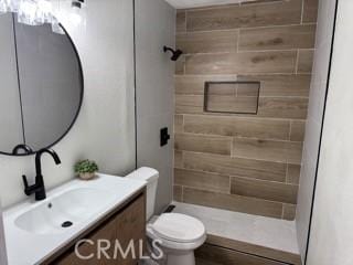 full bath featuring toilet, tiled shower, and vanity