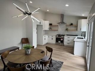 kitchen featuring light wood finished floors, wall chimney exhaust hood, open shelves, a sink, and gas stove