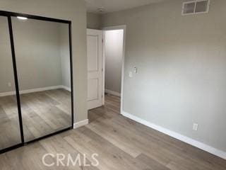 unfurnished bedroom featuring a closet, wood finished floors, visible vents, and baseboards