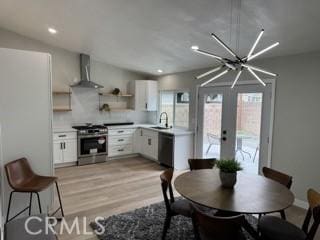 kitchen featuring dishwasher, wall chimney exhaust hood, stainless steel gas range, white cabinetry, and open shelves