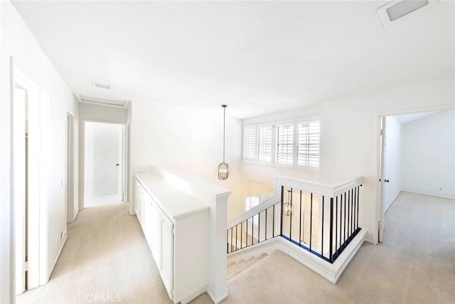 hall with attic access, light carpet, visible vents, and an upstairs landing