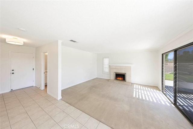 unfurnished living room with baseboards, visible vents, a tile fireplace, light colored carpet, and light tile patterned flooring