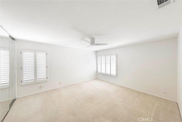 carpeted spare room featuring visible vents and a ceiling fan