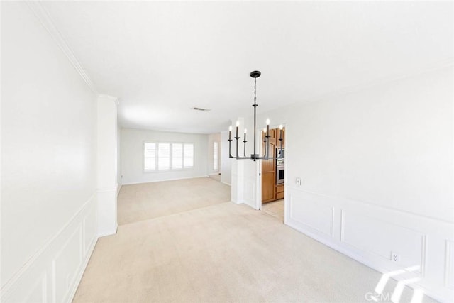 spare room featuring light colored carpet, a decorative wall, visible vents, an inviting chandelier, and crown molding