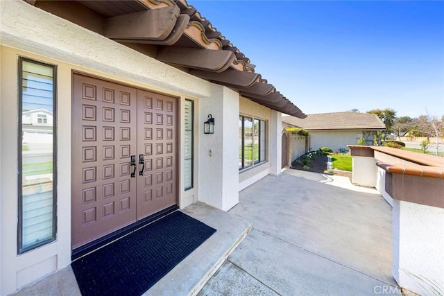 property entrance with a patio area, a tiled roof, and stucco siding